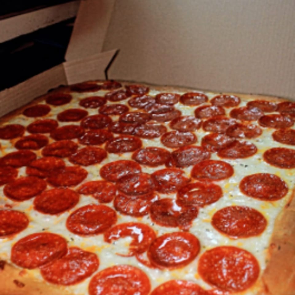 A large, rectangular Capri Pizza pepperoni pizza, covered in cheese and pepperoni, in a cardboard box.