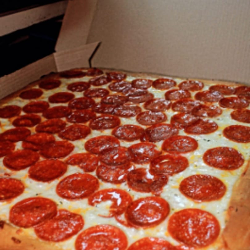 A large, rectangular Capri Pizza pepperoni pizza, covered in cheese and pepperoni, in a cardboard box.