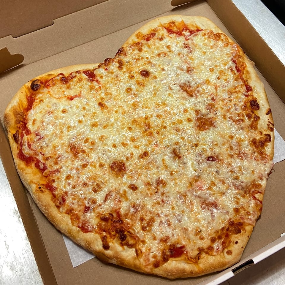 Heart-shaped Capri Pizza with melted cheese and tomato sauce in a cardboard box.