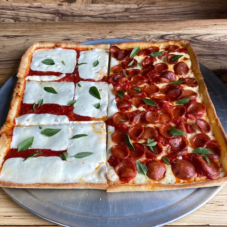 A square Capri Pizza, half with mozzarella and basil, half with pepperoni, on a metal tray.