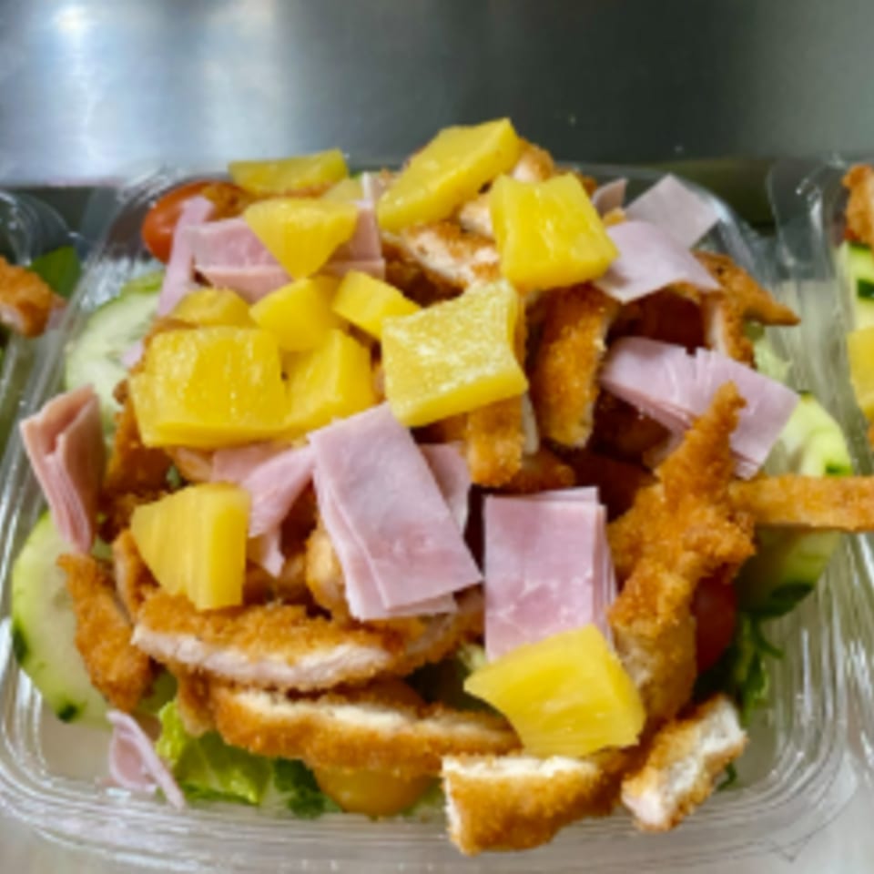 Capri Pizza's salad with crispy chicken, ham, pineapple, and fresh greens in a clear container.